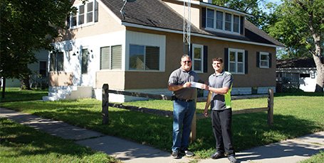 Two people exchange paperwork in front of a home